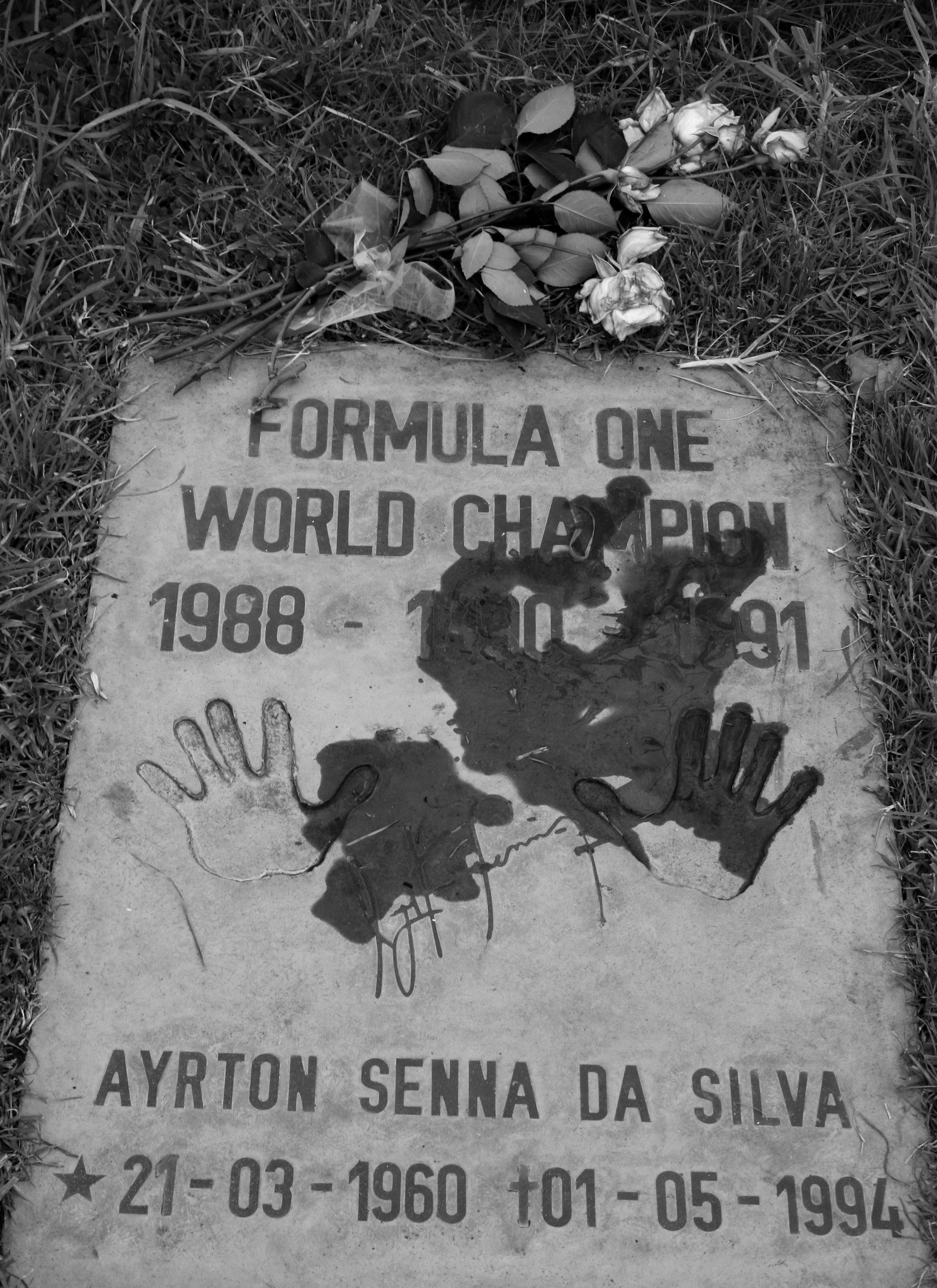 A concrete slab set in grass, lettered ‘Formula One World Champion 1988 – 1990 – 1991’, with two handprints, a signature and a bunch of roses above.