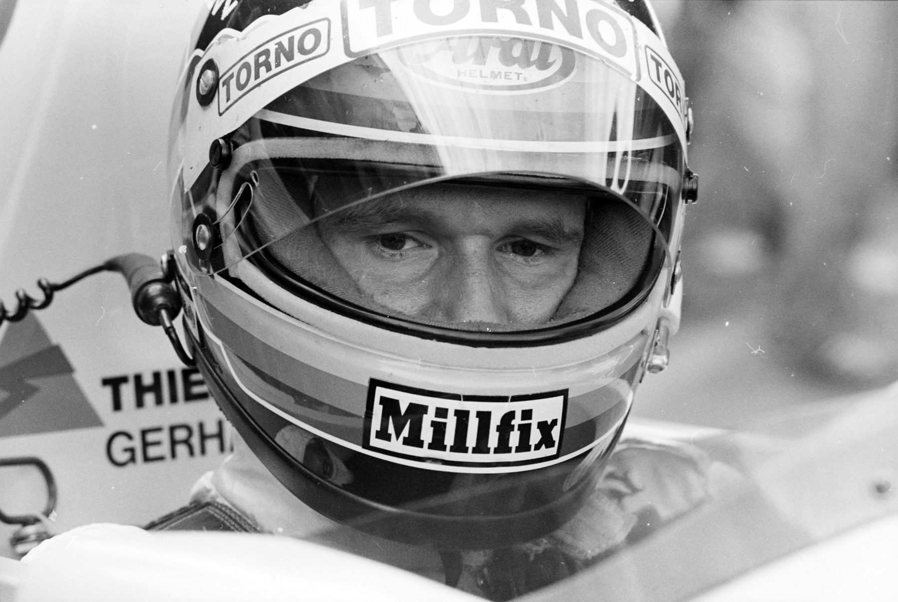 Close-up of a driver in a full-face helmet, visor raised so only his eyes and the bridge of his nose show; the car’s side carries part of the name ‘Gerh’.