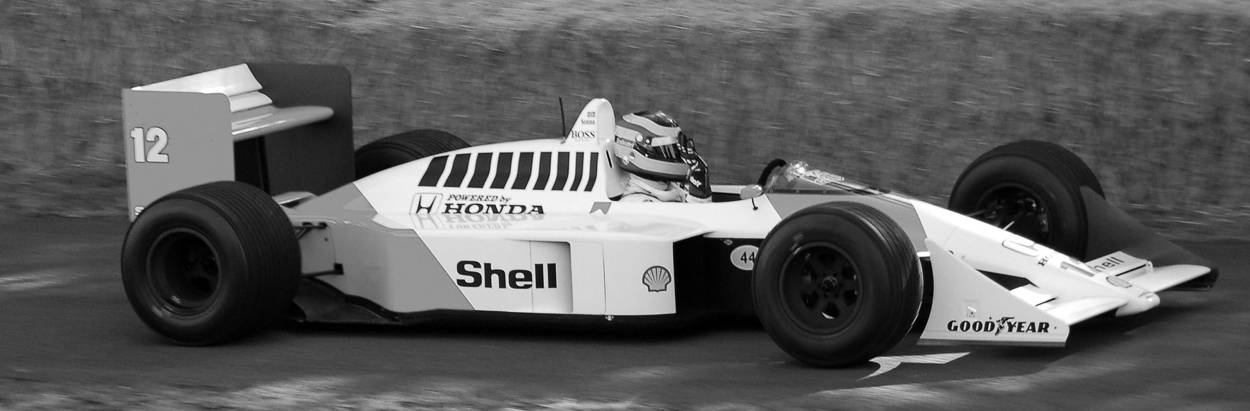 A pale McLaren numbered 12, ‘Shell’ and ‘Honda’ on its flanks, runs past the camera, its driver in a striped helmet, the background a blur.