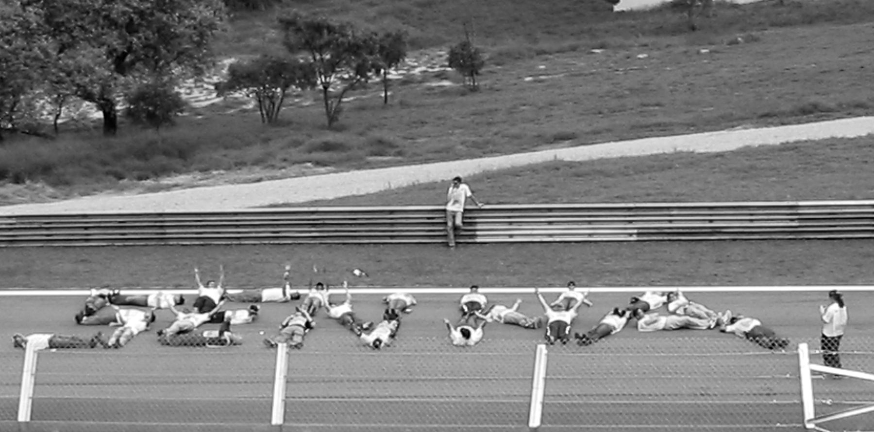 Seen from the grandstand over a fence, a line of people in white lie on the track, their bodies forming the letters of his name.