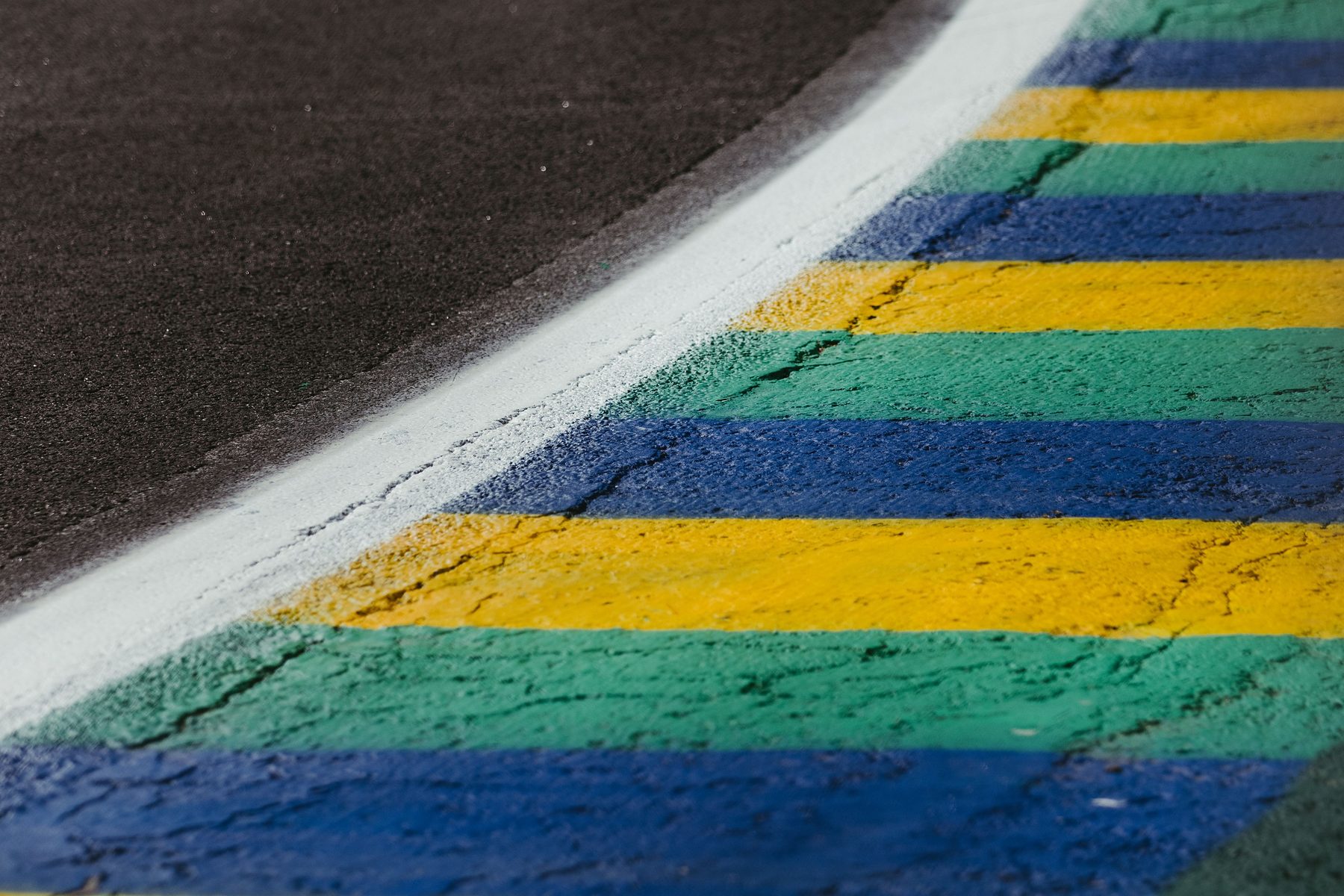 Close-up of a kerb painted in stripes of green, yellow and blue curving along the edge of dark asphalt.