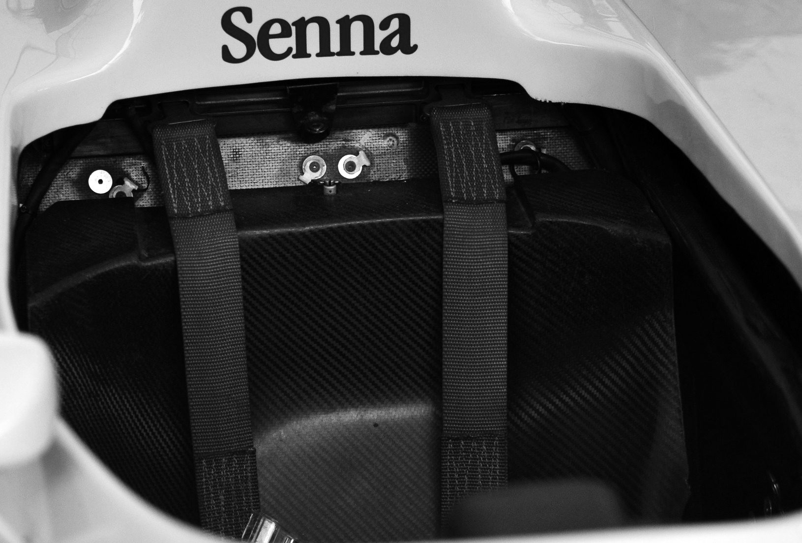Close-up of an empty single-seater cockpit with dark harness straps, the name ‘Senna’ painted on the bodywork just in front of it.