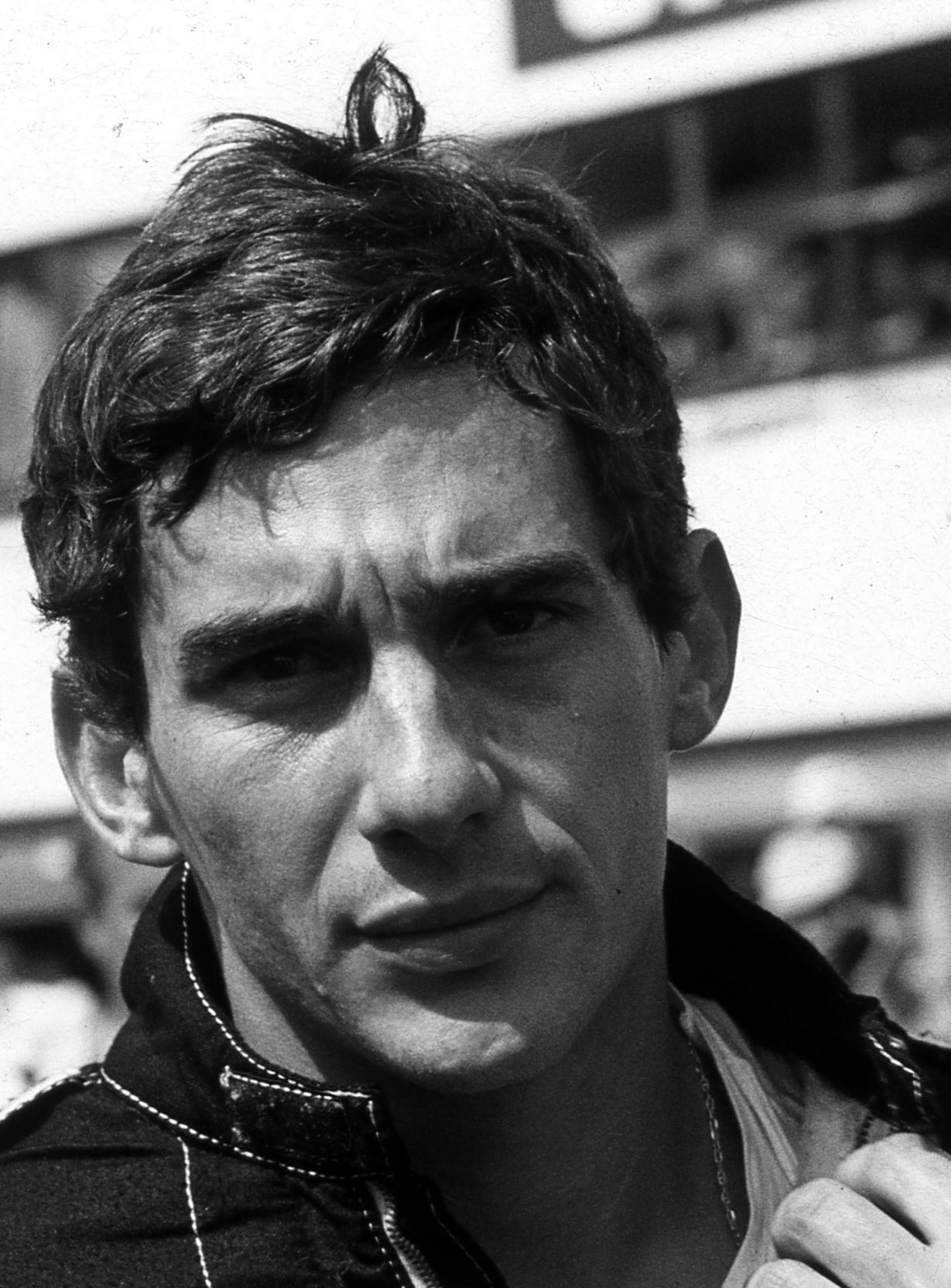 Ayrton Senna in close portrait at 26: tousled dark hair, a level gaze straight into the lens, the collar of his racing overalls open at the neck.